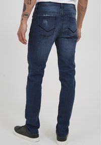 Jeans in denim blu scuro con una vestibilità slim, caratterizzati da leggere abrasioni e una particolare cucitura a zigzag sulle tasche posteriori.