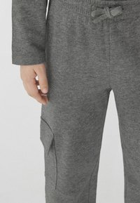 Szare dresy wykonane z miękkiego materiału, z elastycznym pasem ze sznurkiem oraz boczną kieszenią cargo na lewej nodze.