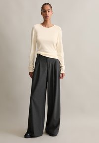 Cremfarbener Longsleeve-Oberteil kombiniert mit hoch taillierten, weiten dunkelgrauen Hosen. Das Outfit zeichnet sich durch eine dezente Textur und eine lässige Passform aus.