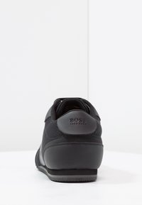 Black sneaker featuring a mix of mesh and synthetic materials, a padded collar, and a rubber sole with branding on the heel.