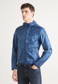 Blaue Kapuzenjacke aus glänzendem, leichtem Material, mit einem Frontreißverschluss und Seitentaschen, im Slim-Fit-Design.