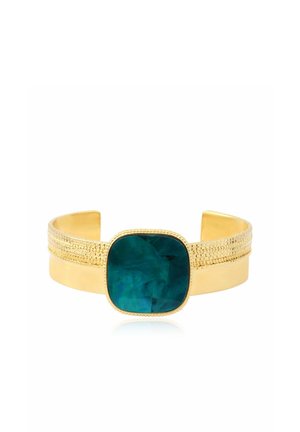 Bracelet manchette en or avec des détails texturés comportant une grande pierre carrée bleu sarcelle foncé au centre sur fond blanc.