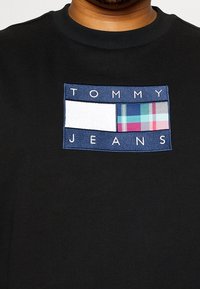 Černá mikina s výšivkou obdélníkové nášivky s nápisem „TOMMY JEANS“ a kostkovanými grafickými prvky v odstínech modré, zelené a růžové.