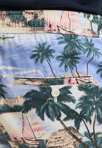 Kleurige tropische shorts met een patroon in blauwtinten, groentinten en roze, versierd met palmbomen, zeilboten en een knoopzak achterop.