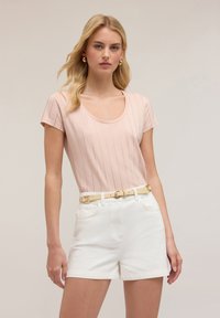 Helles rosa Kurzarmoberteil mit vertikalen Streifen, kombiniert mit weißen Shorts und einem gelben Gürtel mit einer runden Schnalle.