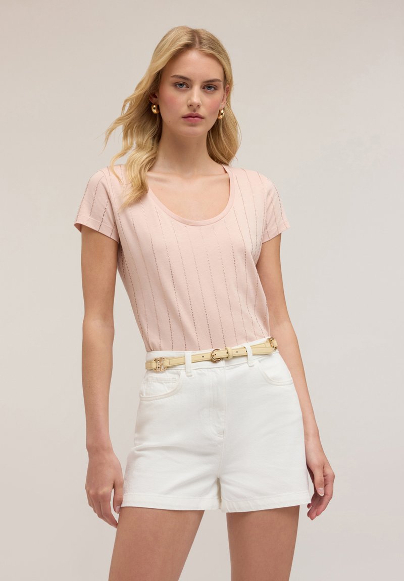 Helles rosa Kurzarmoberteil mit vertikalen Streifen, kombiniert mit weißen Shorts und einem gelben Gürtel mit einer runden Schnalle.