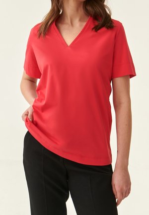 Rotes, kurzärmliges V-Ausschnitt-Shirt mit lockerer Passform und glatter Textur, kombiniert mit schwarzen Hosen. Einfaches, klares Design, ohne Muster oder Akzente.