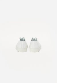 Baskets blanches en cuir avec un design basse, bout arrondi et semelle en caoutchouc blanche. Texture lisse avec des détails de couture subtils à l'arrière.