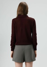 Pull-over en tricot bordeaux à motif losange, doté d'un col et de manches longues, associé à un short gris cintré.