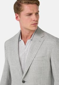 Szary blezer w wzór houndstooth z klapami o prostym kroju, zapinany na jeden guzik i o teksturowym wykończeniu, noszony na jasnoszarym T-shircie polo.