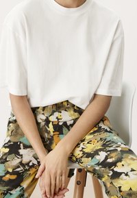 Biała bawełniana koszulka o luźnym kroju zestawiona z wysokim stanem spodni z kolorowym kwiatowym wzorem w zielonym, żółtym i czarnym kolorze.