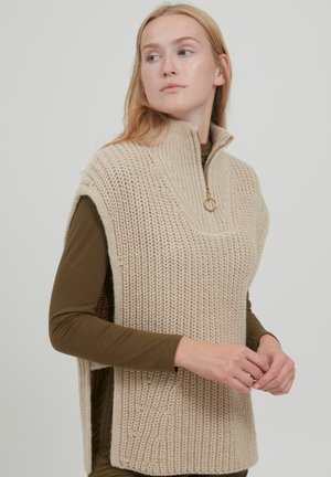 Beige knitted vest with a high collar and zipper detail, featuring a textured pattern and side slits for added comfort.