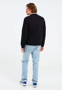 Felpa nera con scollo rotondo classico, abbinata a jeans azzurri chiari. Le scarpe presentano accenti bianchi, grigi e blu. Design semplice.