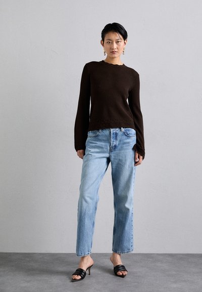 Kahvin rakenteinen pitkähiha sweater, jossa on aaltoileva kaula-aukko, yhdistettynä vaaleansinisiin suoriin farkkuihin ja mustiin korkokenkiin.