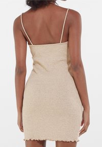 Robe en tricot côtelé beige avec des bretelles fines, silhouette ajustée, ourlet en dentelle et texture douce. La vue arrière montre clairement les détails du design.