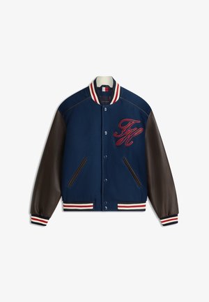 Marineblauw varsityjack met donkerbruine leren mouwen, gestreepte kraag en manchetten, drukknoopsluiting, zakken aan de voorkant en rode geborduurde initialen "TH" op de borst.