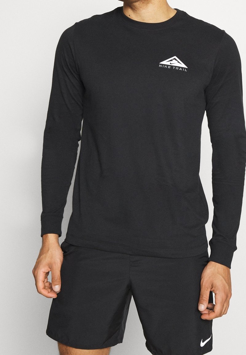 Černé tričko s dlouhým rukávem vyrobené z lehkého materiálu, s bílým logem "Nike Trail" na levém prsu. Hladká textura, design s kulatým výstřihem.
