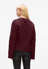 Felpa bordeaux con maniche lunghe e collo tondo, realizzata in tessuto morbido, abbinata a pantaloni in pelle nera aderenti.