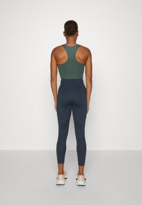 Mörkgrön sporttank topp matchad med högmidjade marinblå tights. Modellen bär också ljusa sneakers.