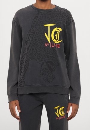 Dunkelgraues Sweatshirt- und Hosen-Set mit schwarzer Leoparden-Grafik und leuchtend gelbem und rotem "JG Milano" Schriftzug auf Brust und Oberschenkel.