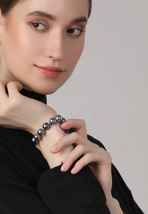 Black bead bracelet featuring glossy, round beads on a wrist, with a smooth texture and subtle shine, contrasted against dark clothing.