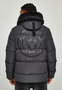 Daunenjacke in Dunkelgrau, mit großem, geprägtem Logo auf dem Rücken, pelzgefütterter Kapuze und gesteppte Abschnitte zur Isolierung.