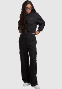 Felpa nera corta con un logo minimalista, abbinata a pantaloni cargo neri dalla vestibilità ampia, con tasche laterali e vita elastica.
