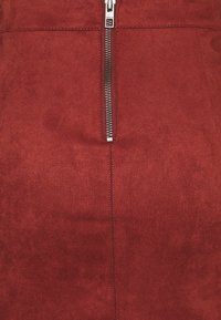 La gonna rossa in suede presenta una chiusura con zip frontale, una superficie liscia e un design aderente con linee pulite e dettagli di cucitura minimi.