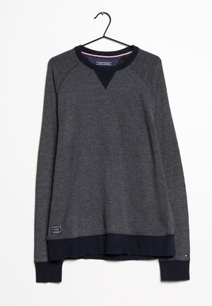 Ciemnoszara bluza z długim rękawem o fakturze waflowej, z granatowymi mankietami, dołem i kołnierzem, powieszona na czarnym wieszaku na białym tle.