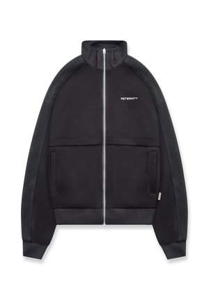 Giacca nera con cerniera, strisce testurizzate sulle maniche, colletto alto, due tasche frontali e testo "RETERNITY" sul petto sinistro.