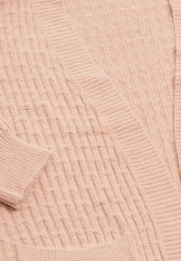 Jemně růžový pletený svetr s žebrovanými manžetami, strukturovaným vzorem copánkového pletení a žebrovaným olemováním kolem výstřihu a předního otevření.