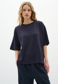 Sötétkék, rövid ujjú póló, laza szabással, kerek nyakkal és puha textúrával. Sötét nadrággal párosítva, minimalista dizájnnal.