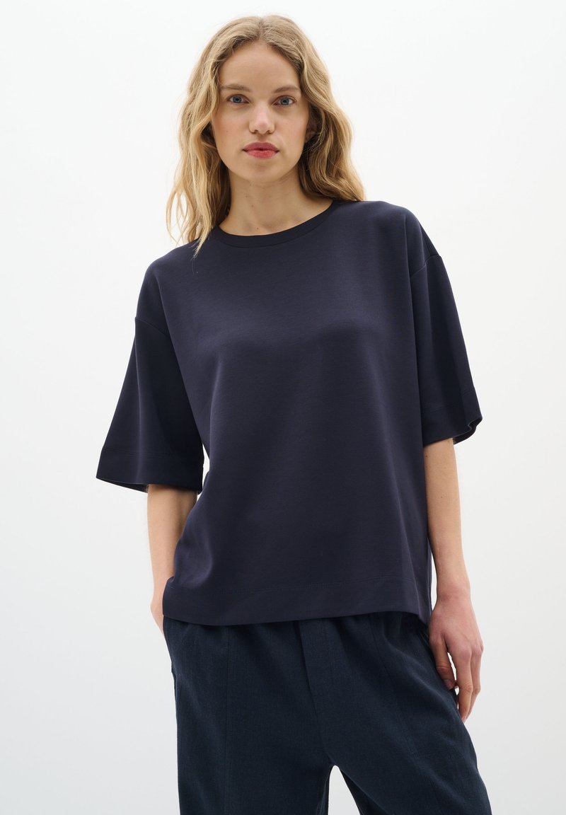 Tamno plava majica kratkih rukava s ležernim krojem, okruglim izrezom i mekanom teksturom. Uparena s tamnim hlačama, minimalistički dizajn.
