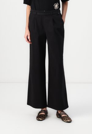 Pantalons noirs à jambes larges avec frente plissé, passants de ceinture et fermeture à double bouton à la taille. Portés avec des ballerines imprimées léopard.