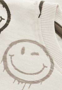 Helle Stoff mit strukturierter Oberfläche, versehen mit grauen Smiley-Gesichtsdrucks und einem gerippten Kragen. Bemerkenswert für sein lässiges Design.