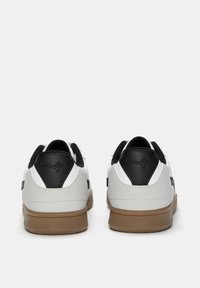 Weiße und schwarze Sneaker mit einem Obermaterial aus strukturiertem Leder und Wildleder, Gummisohle und kontrastierenden Akzenten an der Ferse und den Seiten.