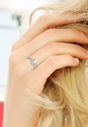 Bague en argent avec des détails intricats et une pierre précieuse transparente centrale, portée sur une main reposant contre des cheveux blonds.