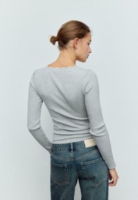 Sivi rebrasti dugi rukav top s nazubljenim izrezom, uparen s plavim trapericama koje na stražnjem pojasu imaju oznaku.