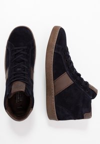 Vysoké tenisky v námořnické nubukové kůži s hnědými akcenty, s texturovanou gumovou podrážkou, kulatou špičkou a kontrastním designem bočního pruhu.