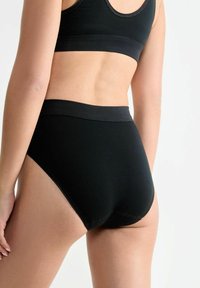 Schwarze hochtaillierte Unterwäsche mit einem glatten, elastischen Bund und weichem Stoff, der subtilen Nähten entlang der Kanten aufweist.