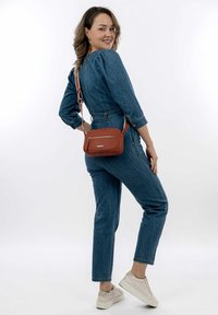Denim jumpsuit with puff sleeves, paired with a small rust-colored crossbody bag featuring a zipper and textured surface. Light sneakers.