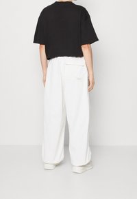 Svart, kortärmad t-shirt som kombineras med vita, vida byxor med en bakficka. Outfiten har en avslappnad passform och en enkel struktur.