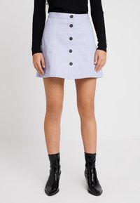 Ljuslila, knäppt kjol i mjukt material, med fem mörka knappar, utsvängd form och sidofickor. Stylad med svarta stövlar.