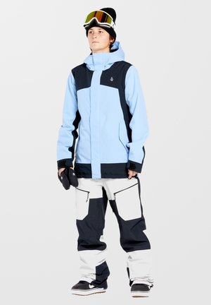 Light blue waterproof snowboard jacket with black accents, paired with white and black snow pants featuring zippered pockets and a relaxed fit.