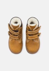 Botas infantiles de cuero marrón con dos correas de Velcro, forro de forro polar, puntas redondeadas y costura blanca contrastante alrededor de las suelas.