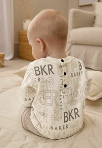 Dug rukavi kremasti top s sivim printanim slovima, uključujući "BAKER," s okruglim izrezom i tri crna dugmeta na leđima.