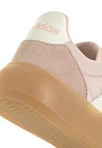 Zapatilla rosa claro con acentos en blanco y beige, con un talón de ante, parte superior de sintético liso y una suela translúcida texturizada.