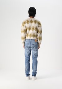 Suéter de punto en crema con un patrón en zigzag verde, combinado con jeans de color azul claro y zapatillas blancas. La textura parece esponjosa y acogedora.