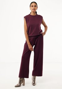 Top burdeos sin mangas combinado con pantalones de pierna ancha burdeos. Botines metálicos y una textura suave en todo.
