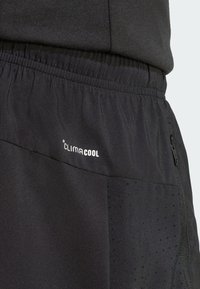 Pantalones cortos deportivos negros con cintura elástica, bolsillo lateral con cremallera, panel de ventilación perforado y marca "climacool" en la tela.